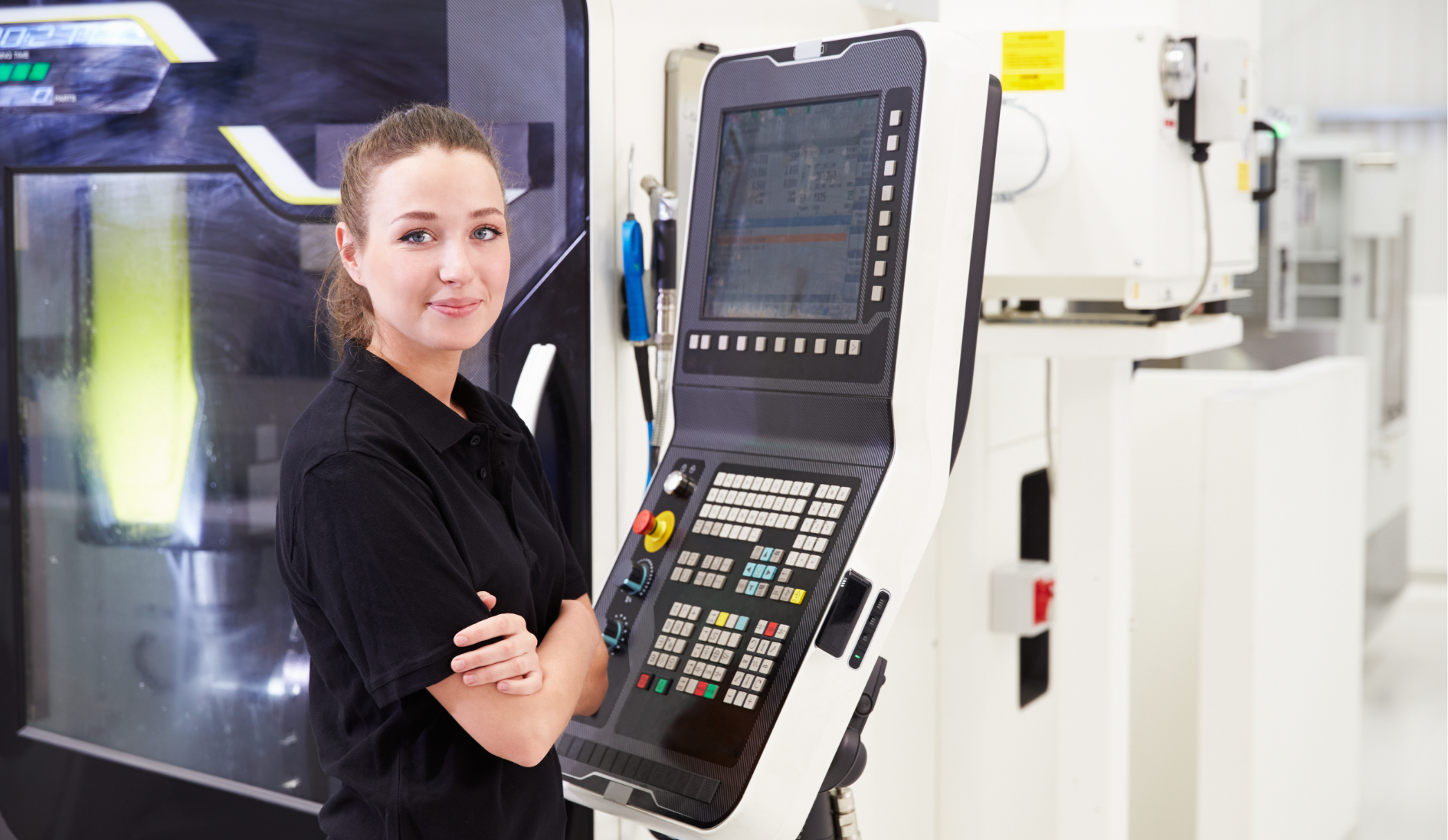 En kvinna står vid en cnc-maskin och ler mot kameran